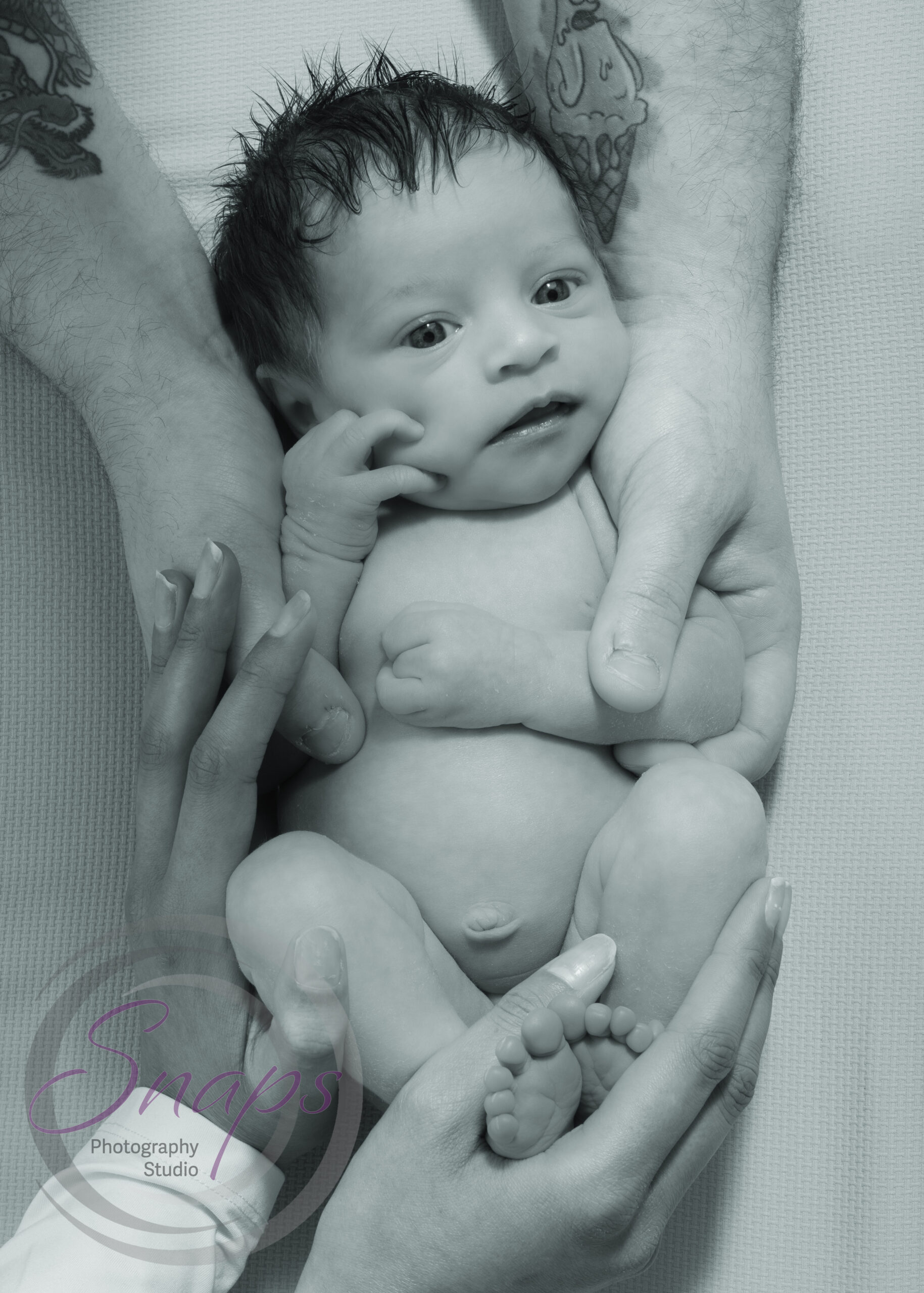 black and white photo of parents hands around baby holding her