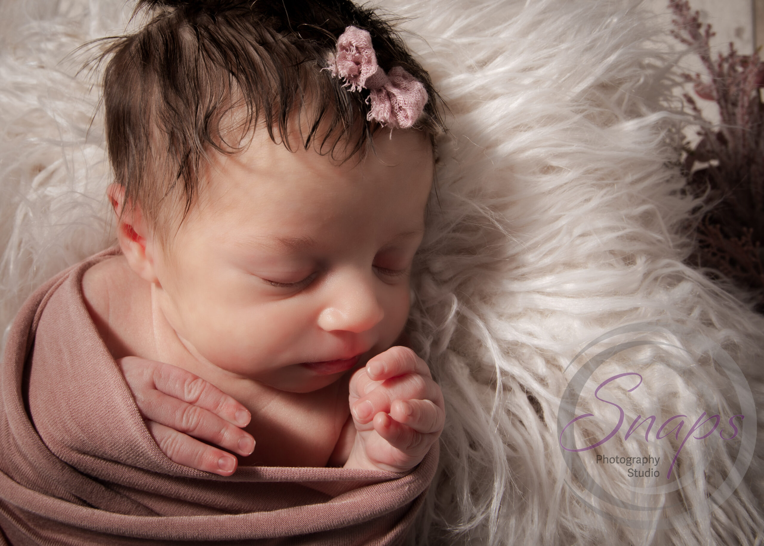 newborn baby girl sleeping on white fluff in a pink wrap