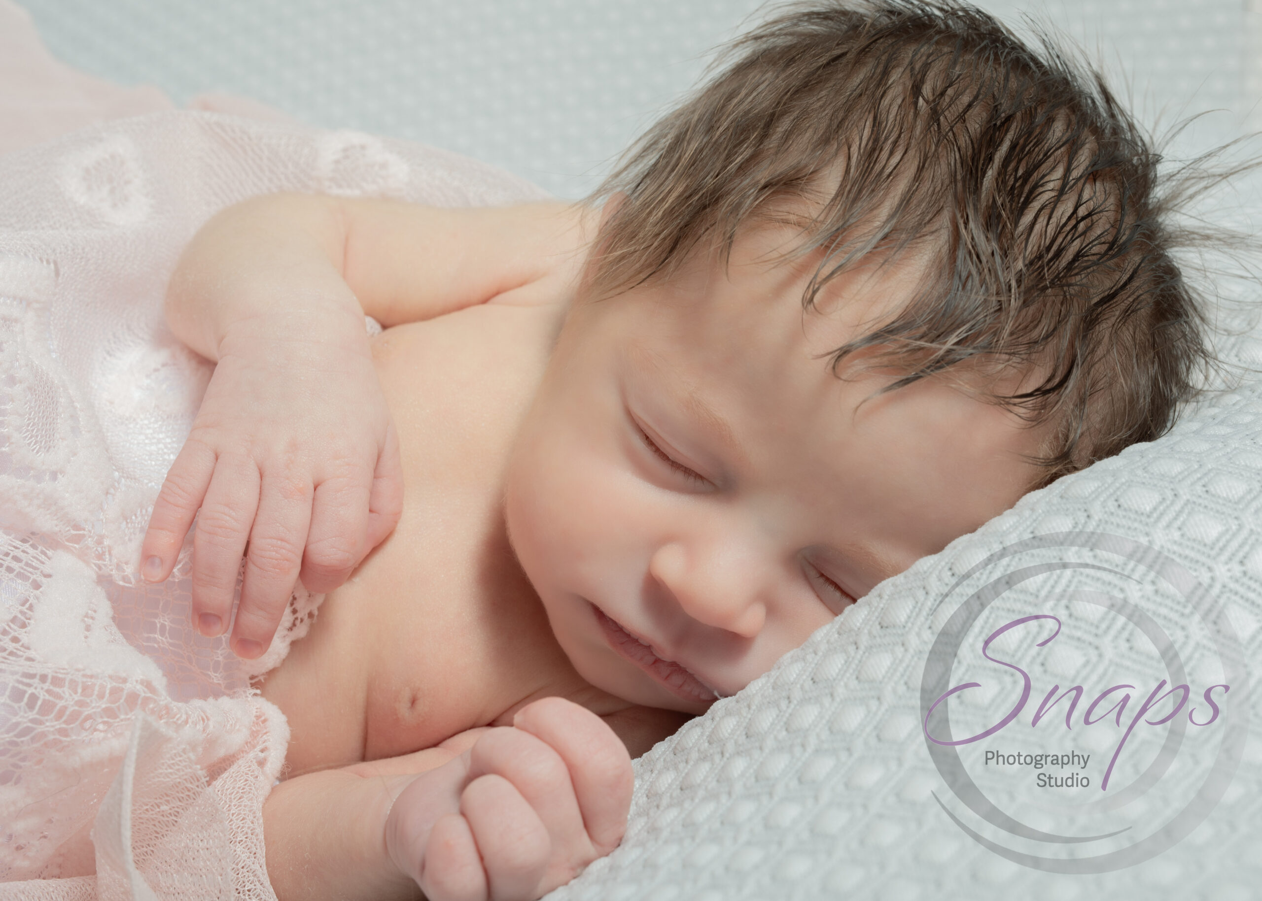 newborn baby sleeping on a grey bed with a pink blanket