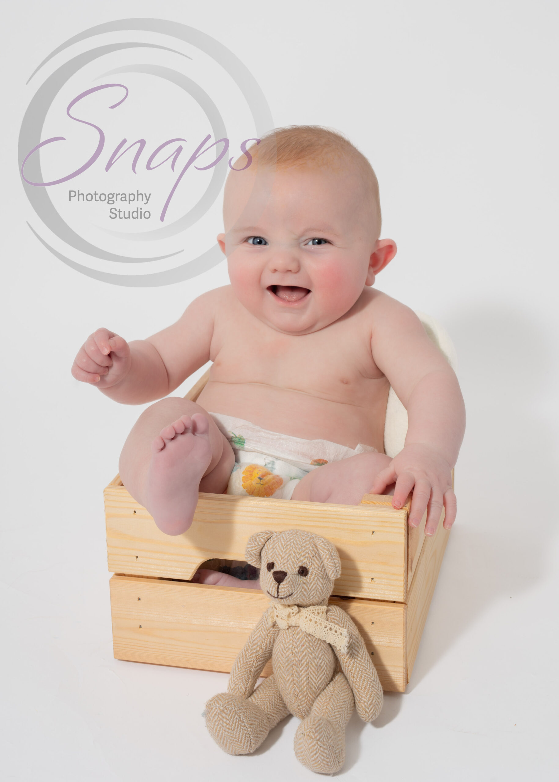 baby boy in a wooden box with a little bear laughing