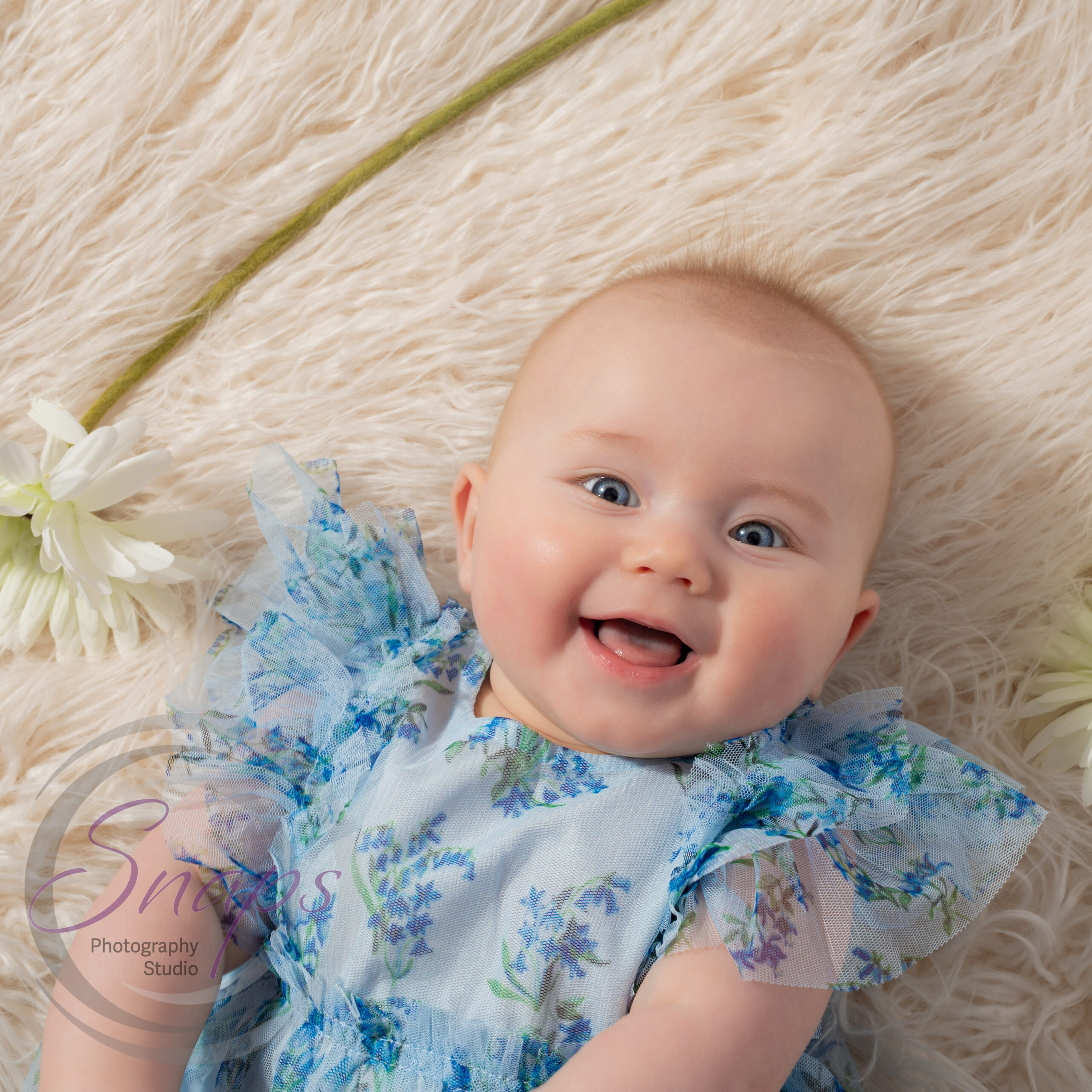 baby in a blue dress smiling with a flower
