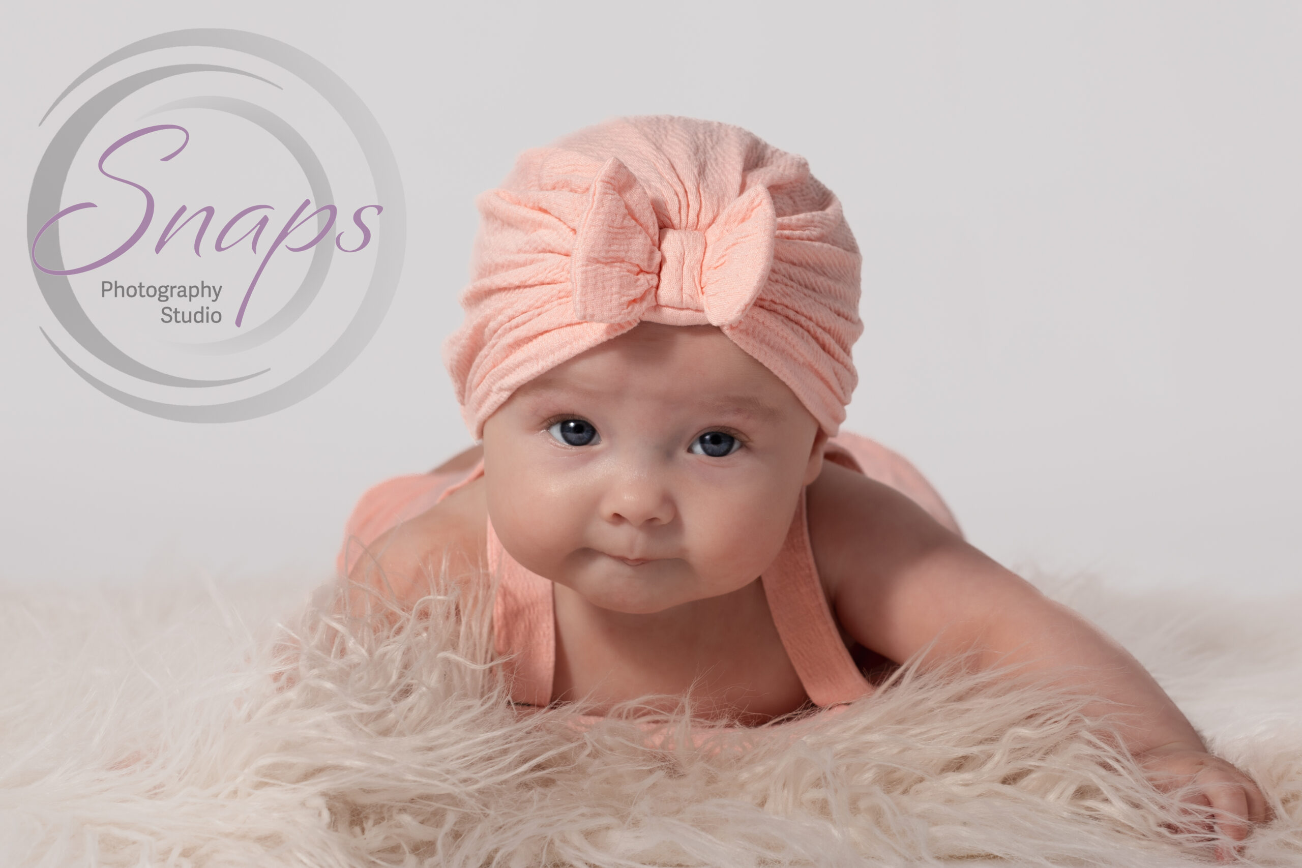 little girl doing tummy time wearing pink on white fluff