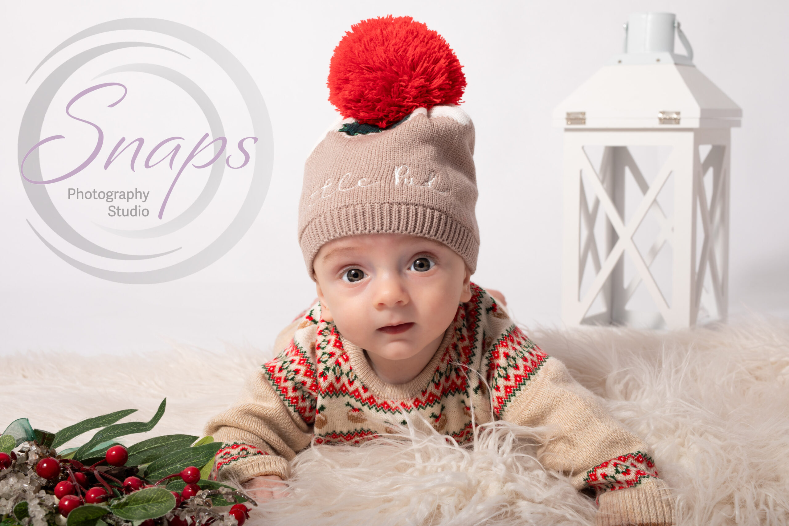 Christmas themed tummy time with baby boy wearing bobble hat with Christmas props