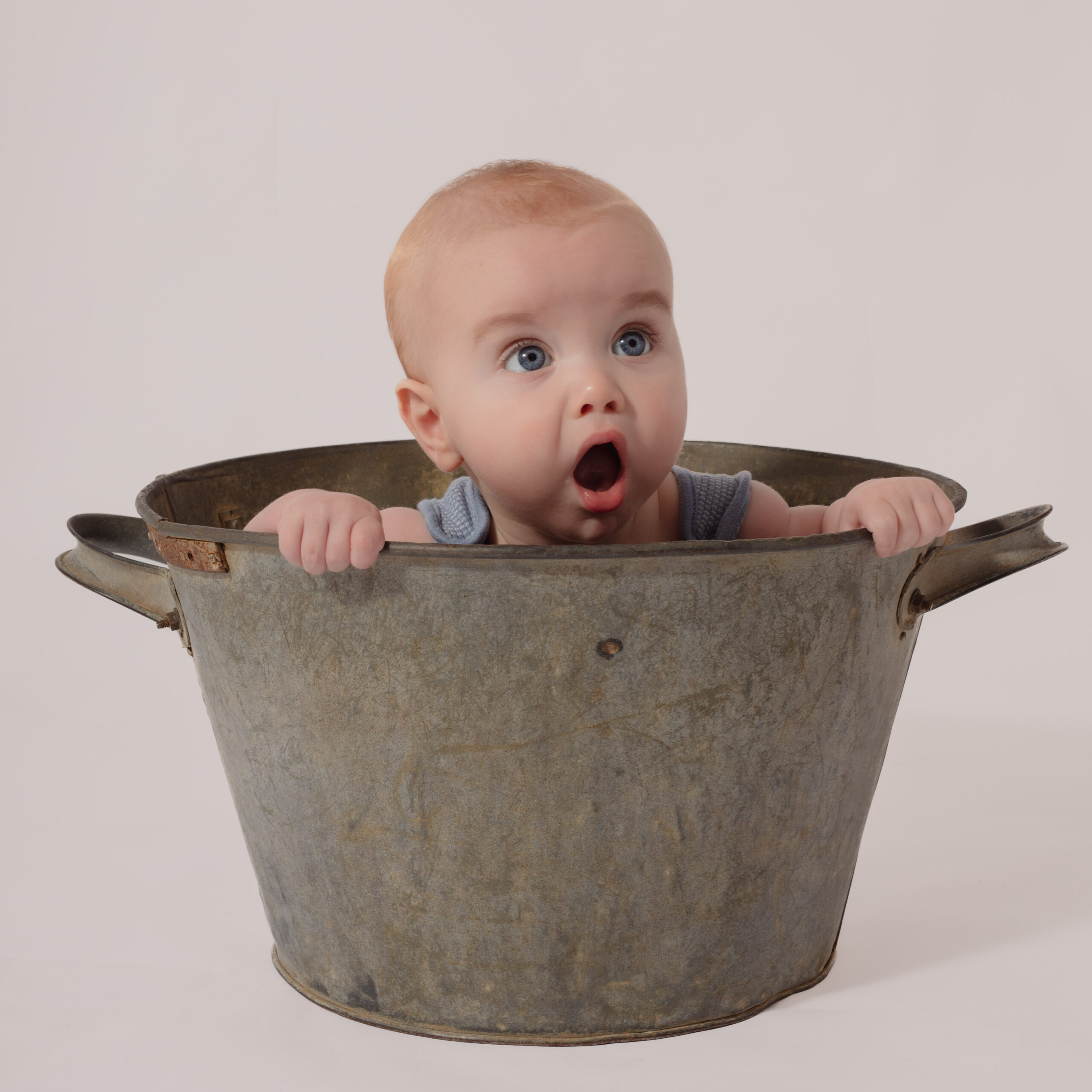 Baby boy in a bucket, holding onto the side with his mouth open