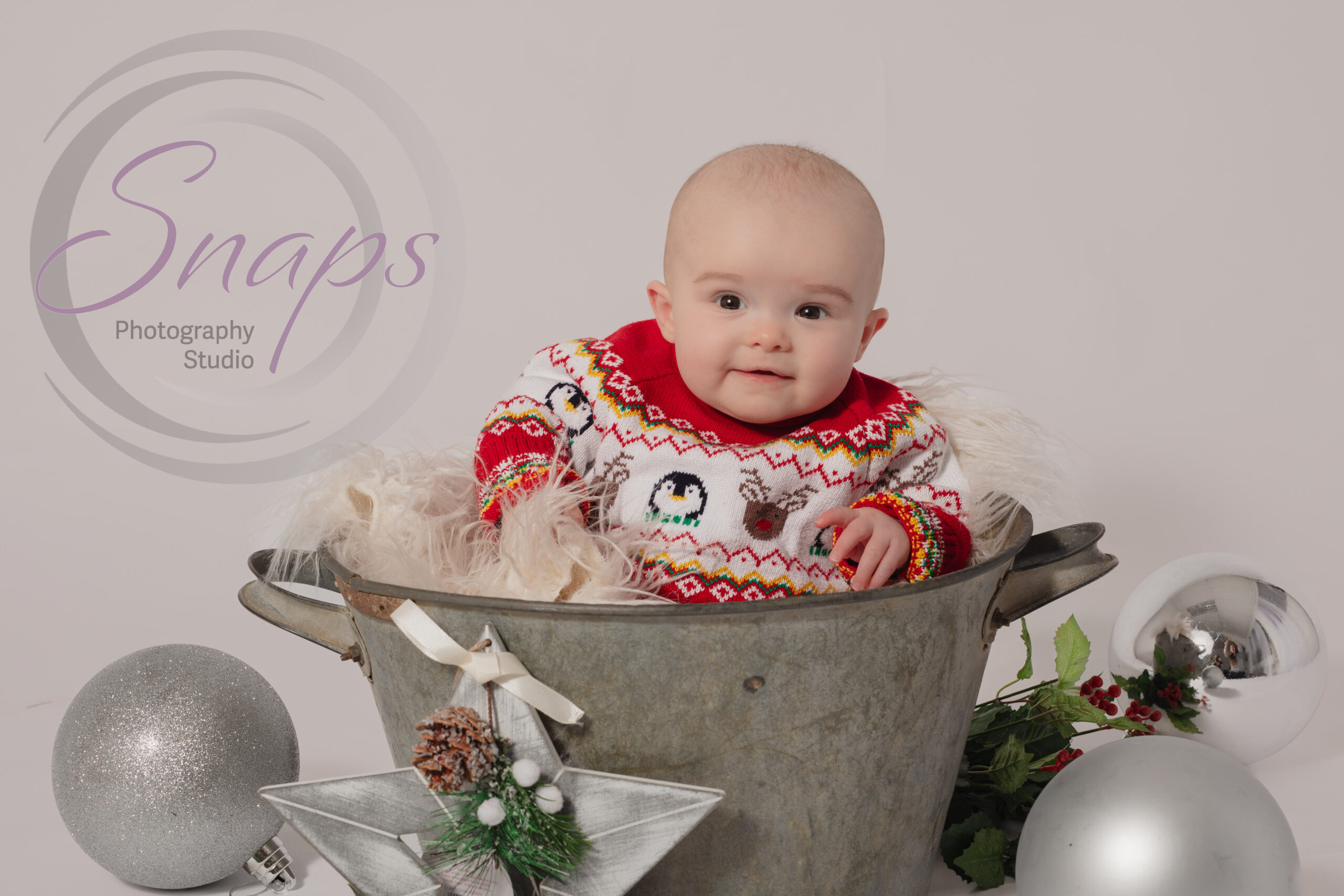 festive baby girl in a bucket with Christmas decorations around her wearing a Chrismtas jumper