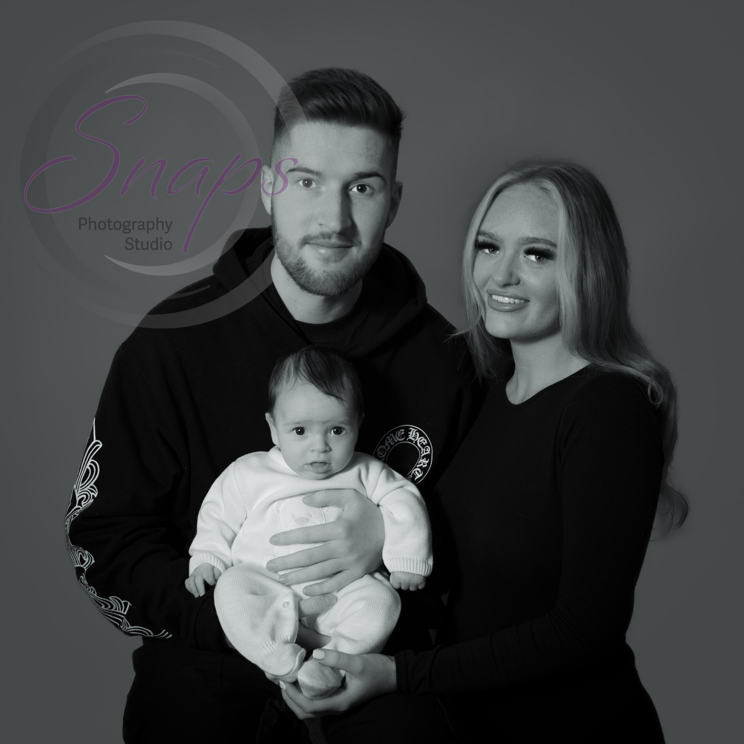 mummy, daddy and baby smiling at the camera in black and white photo