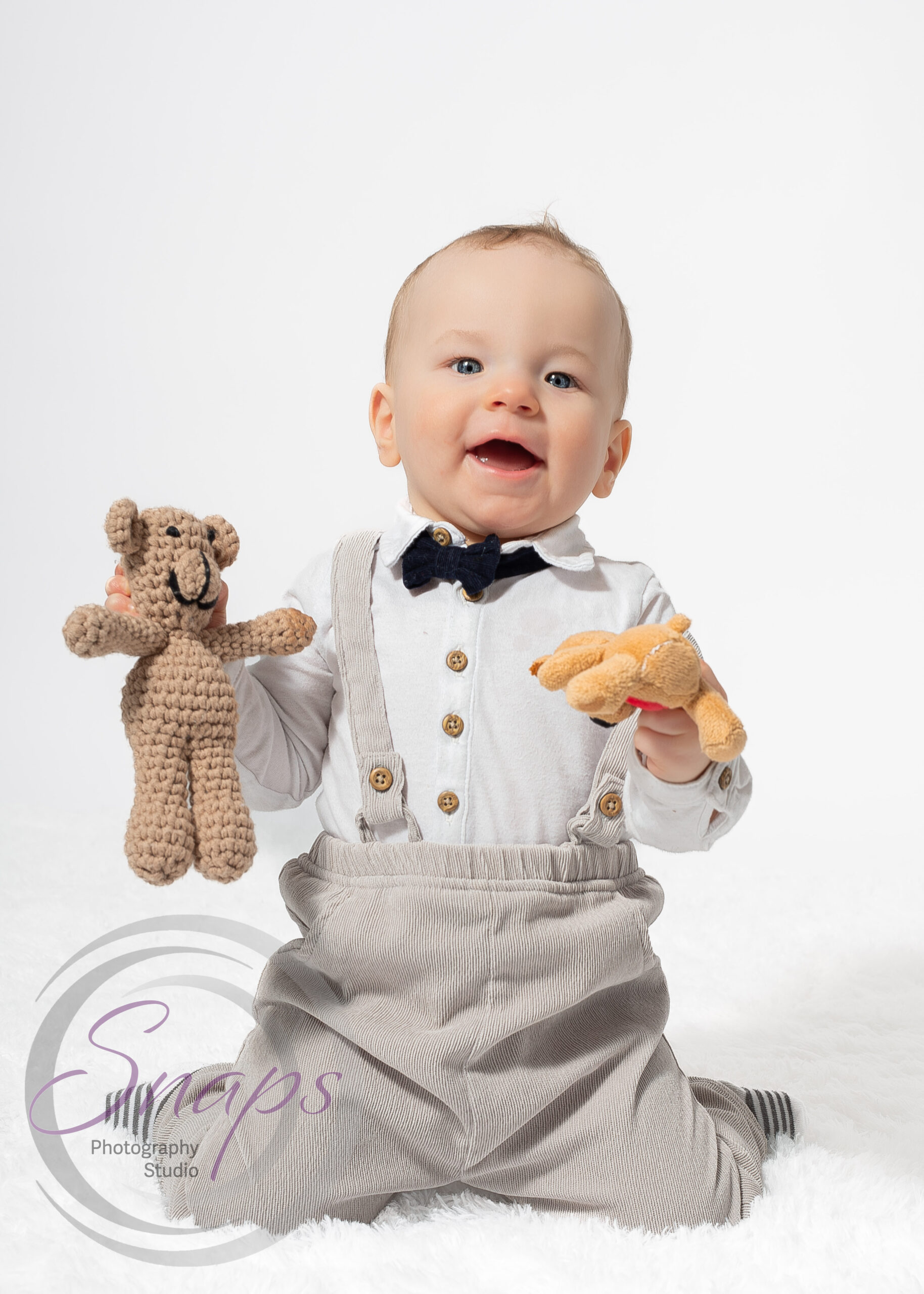 happy baby boy wearing bow tie holding teddy bears