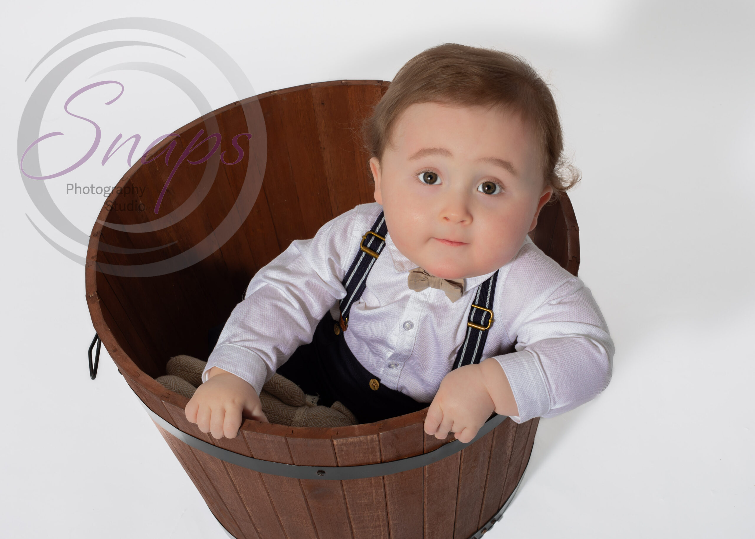 smart little boy in a wooden bucket looking up at the camera