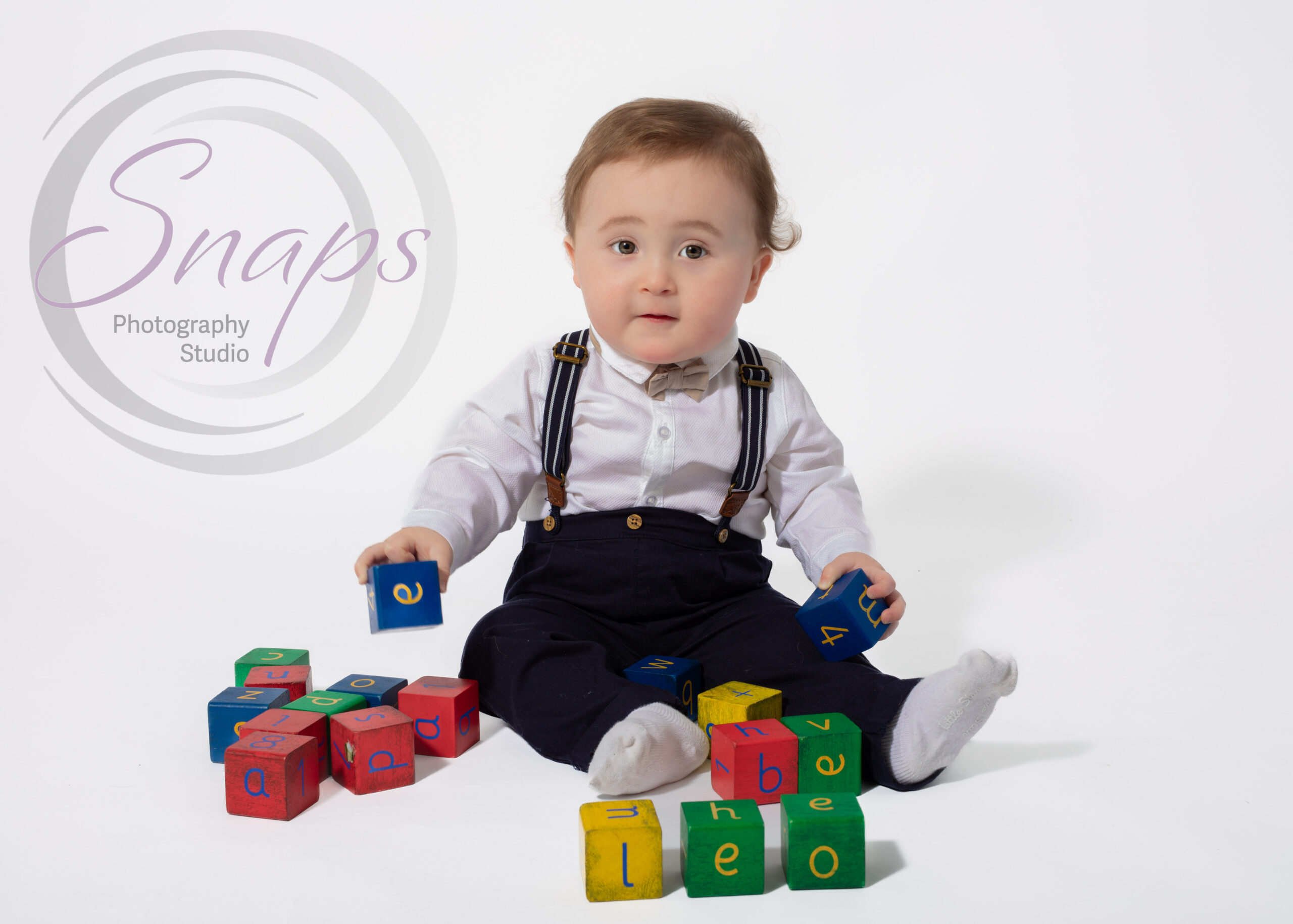 little boy in dungarees and a bow tie playing with blocks