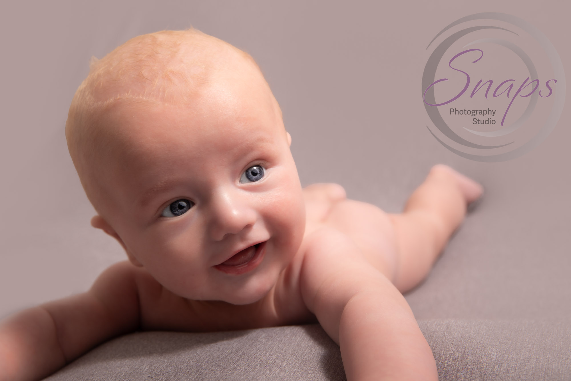 Baby boy doing tummy time and smiling at a photoshoot in stroud